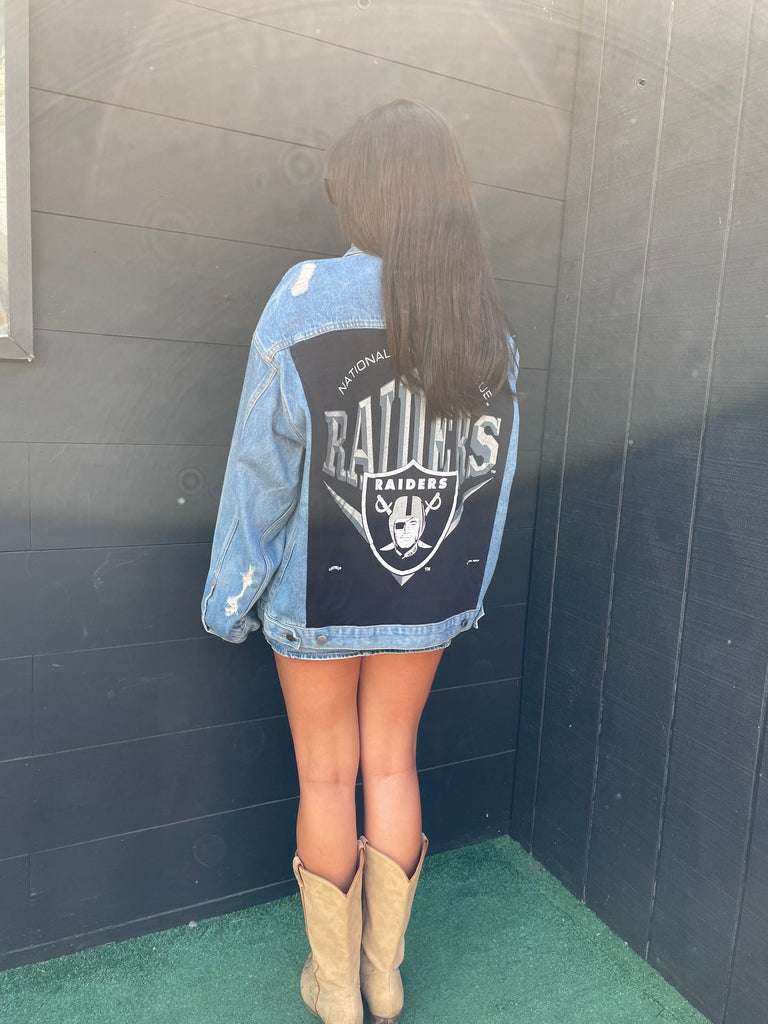 Person wearing a denim jacket with a logo, standing on a wooden floor.
