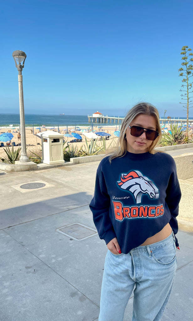 Person wearing a navy blue Broncos sweatshirt by the beach